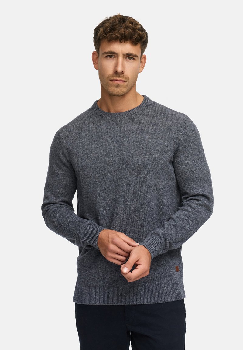 Pull gris avec un col rond et des manches longues, présentant un motif en tricot texturé et des bords côtelés au niveau des poignets et de l'ourlet. Détail de petit logo en bas.