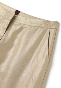 Pantaloni metallici dorati con una superficie liscia, con plissettature e tasche laterali. La vita presenta un'etichetta con il marchio in rosso e nero.