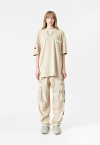 Camiseta oversized de pana beige con un bolsillo en el pecho, combinada con pantalones cargo a juego que cuentan con múltiples bolsillos y un corte relajado.