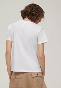 T-shirt bianca in cotone a maniche corte con vestibilità rilassata, collo arrotondato e design semplice. Indossata con pantaloni cargo beige con tasche.