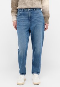 Jeans de mezclilla de color azul claro con un corte relajado, cintura alta y detalles de desvanecimiento sutil. Combinados con zapatillas blancas para un contraste.
