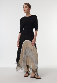 Top negro acanalado con mangas cortas combinado con una falda plisada con colores beige y negro, detalle de encaje y texturas en capas. Sandalias negras.