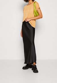 Zwarte satijnen rok met een oranje T-shirt met korte mouwen, aangevuld met een groene tas en chunky zwarte schoenen. Soepele texturen en een relaxte pasvorm.