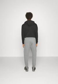 Svart huvtröja med snörning och grå joggingsbyxor med elastisk midja och sidofickor, bärs med svarta sneakers.