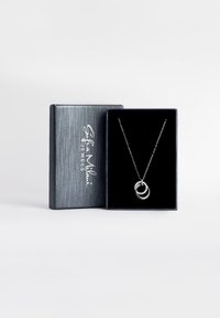 Sølvhalskæde med sammenflettede ringe; en ring har små klare sten. Præsenteret i en sort fløjlskasse med et sølvlogo.