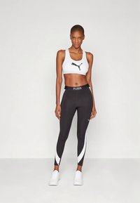 Zwarte sportlegging met witte zijaccenten en een tailleband met de tekst "PUMA", gecombineerd met een witte sportbeha met een zwart logo.