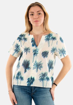 Blouse blanche à manches courtes avec imprimé palmiers bleus, décolleté en V, tissu léger et coupe décontractée, associée à un jean en denim bleu.