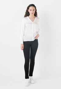 Blusa blanca de manga larga con un sutil escote en V, combinada con pantalones ajustados negros y zapatillas blancas, presentando una textura suave y un diseño entallado.
