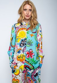Buntbedrucktes Lounge-Outfit, das eine Mischung aus lebhaften Mustern zeigt, darunter Blumen, Sonnen und abstrakte Designs in Blau, Pink und Gelb.