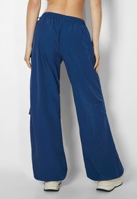 Navy blue, lightweight wide-leg pants with an elastic waistband and side pockets, shown from the back. Smooth texture, casual design.