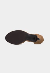 Καφέ σουέντ ψηλοτάκουνο παπούτσι εμφανιζόμενο από τη σόλα, με μαύρο πάτο και καμπυλωτή φτέρνα, πάνω σε απλό λευκό φόντο.