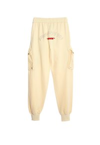 Pantalones de chándal color crema hechos de una tela suave, con puños elásticos, bolsillos laterales tipo cargo y texto bordado en gris y rojo.