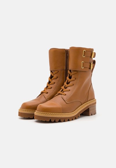 Brown leather ankle boots with laces, a side zipper, and two gold buckles. Features a textured grip sole and a low stacked heel.