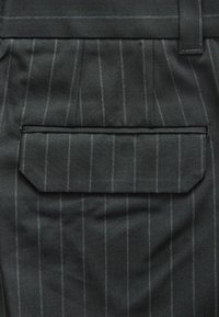 Tissu en chevrons gris foncé avec des rayures blanches. Comprend une poche arrière rectangulaire avec un rabat et une couture horizontale au-dessus.