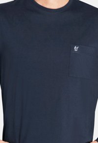 Dunkelblaues T-Shirt aus weichem Baumwollstoff. Verfügt über einen runden Halsausschnitt und eine Brusttasche mit dezenten gestickten Logo-Details. Glatte Textur.