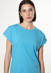Blå bomulds t-shirt med korte rullede ærmer, rund halsudskæring, afslappet pasform og glat tekstur, præsenteret mod en lys baggrund.