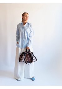 Chemise bleu clair boutonnée, pantalon blanc à jambes larges, et sac imprimé léopard avec des accents noirs. Des chaussures plates bleues complètent la tenue.