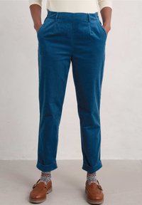 Pantaloni in corduroy blu con una vestibilità comoda, dotati di tasche sui lati e orli arrotolati. Indossati con mocassini marroni e calze a motivi.