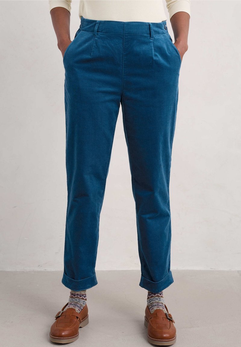 Pantaloni in corduroy blu con una vestibilità comoda, dotati di tasche sui lati e orli arrotolati. Indossati con mocassini marroni e calze a motivi.