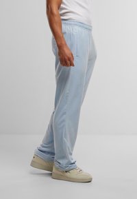 Pantaloni della tuta azzurri chiari realizzati in tessuto morbido, con vita elastica e tasche laterali, con dettagli di cucitura sottili lungo le cuciture.