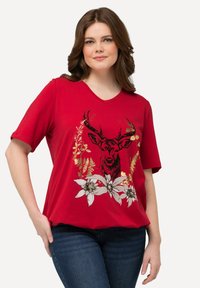 Camiseta corta roja de manga corta con un gráfico de ciervo negro rodeado de diseños florales en tonos blanco y dorado. Escote en forma de V y corte holgado.