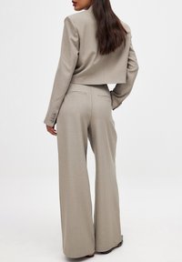 Heled beež värvitoonik, millel on üks lõhe, koos kõrge vöökohaga, laiade pükstega. Sile tekstuur ja diskreetsed õmbluse detailid.