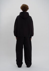 Zwarte oversized hoodie met een kangoeroezak en een verstelbare trekkoord, gecombineerd met losse zwarte broek. Glad textuur, casual ontwerp.