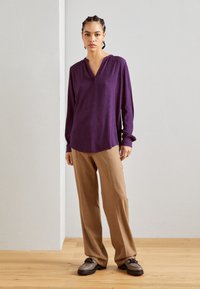 Purple long-sleeve blouse with a V-neckline, textured fabric, paired with beige wide-leg trousers and grey lace-up shoes.