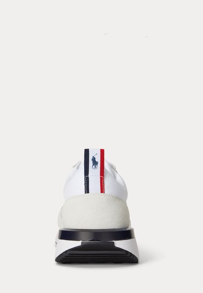 Adidași albi văzuți din spate cu talpă neagră, călcâi din piele intoarsă și o etichetă roșie, albă și albastră cu logo-ul unui jucător de polo.