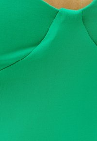 Groene geribbelde stof met een gladde textuur, voorzien van een gebogen halslijnontwerp. Het materiaal heeft een consistente kleur en een lichte glans.