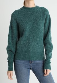 Vihreä neulepaita, jossa on pyöreä kaula-aukko, ribbetyt hihansuut ja helma. Pehmeä, tekstuuri materiaali, rento malli ja raglan-hihat.