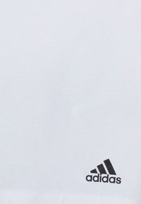 T-shirt en coton blanc avec un logo Adidas noir dans le coin inférieur droit. Le tissu est lisse avec un design simple et épuré.