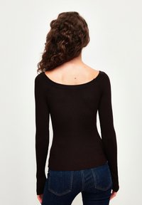 Haut à manches longues en brun foncé à côtes, avec un décolleté large, une silhouette ajustée et une texture douce, associé à un jean bleu foncé.