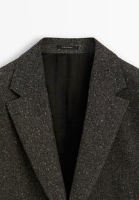 Dunkelgrauer Blazer aus strukturiertem, glitzerndem Stoff mit Reverskragen und schwarzem Futter. Das Etikett im Inneren trägt die Aufschrift "MADE IN PORTUGAL."