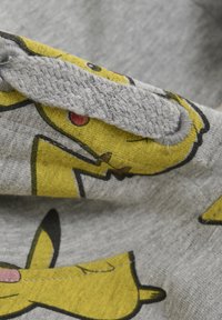 Grauer Stoff mit einem bedruckten Design eines gelben Cartoon-Charakters mit roten Akzenten und schwarzen Konturen. Die Textur wirkt weich und gewebt.