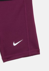Nike šortse u tamnoljubičastoj boji, s bijelim logotipom i kontrastnim crnim pojasom. Izrađene od rastezljivog materijala s vidljivim šavovima.