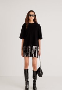 Czarny oversize'owy t-shirt, mini spódniczka z cekinami o naprzemiennych srebrnych i czarnych wzorach, zestawiona z błyszczącymi czarnymi kozakami za kolano oraz małą torebką.
