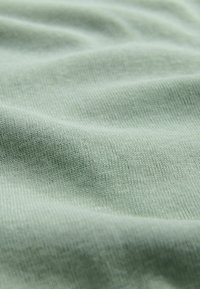 Tissu tricoté doux vert clair avec une fine texture côtelée visible et des plis délicats créant des ombres subtiles.
