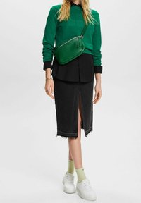Sudadera verde, camisa negra con botones, falda de mezclilla negra con una abertura frontal, zapatillas blancas y un bolso cruzado verde.