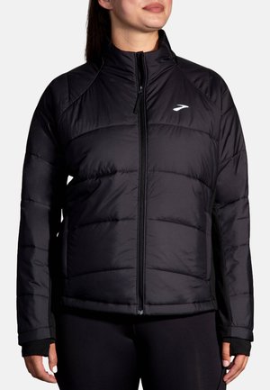 Čierna puffa bunda s prešívaným vzorom, vysokým golierom a úplným zipsom. Obsahuje logo na hornej ľavej strane a elastické manžety pre lepšie priliehanie.