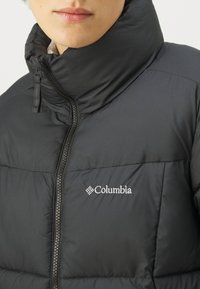 Czarna kurtka puchowa z wysokim kołnierzem, zapięciem na zamek i logiem Columbia. Gładka faktura, pikowane panele i subtelny błyszczący wykończenie.