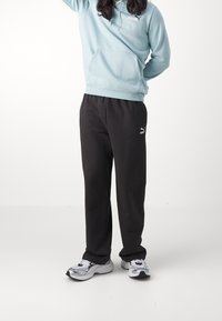 Vaaleansininen huppari, jossa on etutasku ja kiristysnyöri, yhdistettynä mustiin collegehousuihin, joissa on valkoinen logo. Valkoiset ja mustat lenkkarit täydentävät asun.