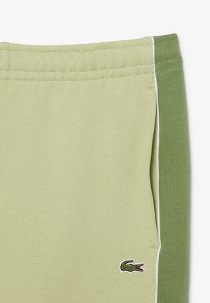 Lichtgroene shorts met een olijfgroen zijpaneel en witte bies, een elastische tailleband en een klein geborduurd krokodillenlogo bij de zak.