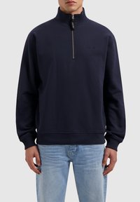 Navy zip-up sweatshirt with high collar, ribbed cuffs, and hem. Soft fabric, minimal branding on the chest, and a functional zipper.