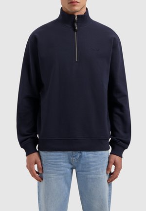 Marineblaues Zip-Hoodie mit hohem Kragen, gerippten Bündchen und Saum. Weiches Material, dezente Markierung auf der Brust und ein funktionaler Reißverschluss.