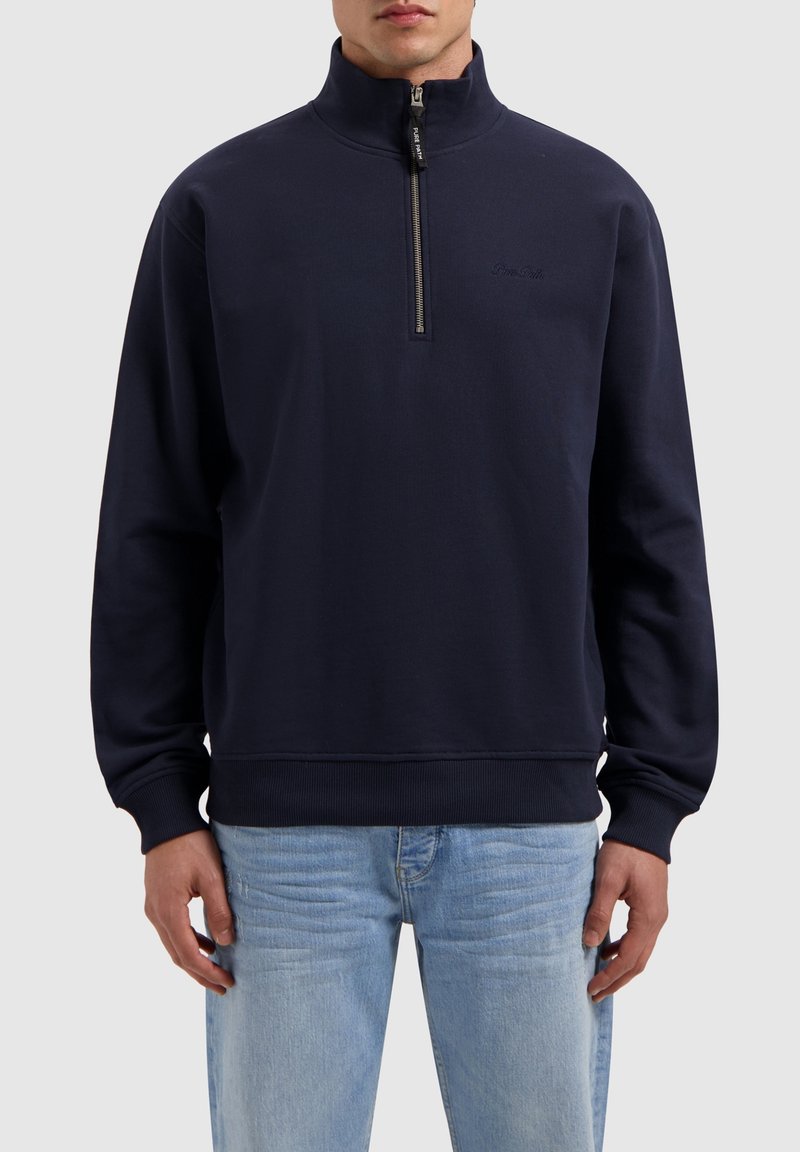 Navy zip-up sweatshirt with high collar, ribbed cuffs, and hem. Soft fabric, minimal branding on the chest, and a functional zipper.