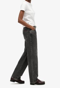 Jeans negros de tiro alto y corte recto con textura descolorida, combinados con una camiseta blanca ajustada y mocasines granate con suela texturizada.