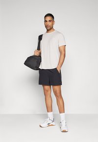Lys grå kortermet t-skjorte, mørke shorts, hvite joggesko, teksturert stoff, og svart treningsbag. Enkel design, uten mønstre.