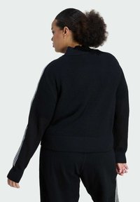 Čierny textúrovaný pletený sveter s vysokým golierom, s tromi bielymi pruhmi na rukávoch a rebrovanými manžetami a spodným okrajom.