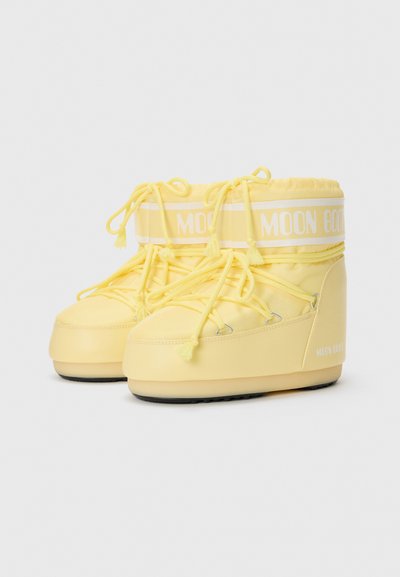 Yellow winter boots with a soft texture, featuring a lace-up design, elastic bands, and a padded collar. Logo printed in white accents.